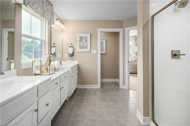 full bath with a tile shower, tile patterned floors, double vanity, a sink, and baseboards