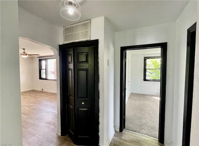 hall featuring baseboards, wood finished floors, and arched walkways