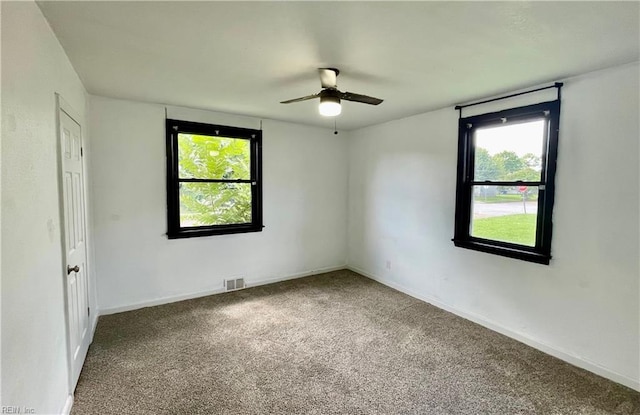 carpeted spare room with visible vents, a ceiling fan, and baseboards