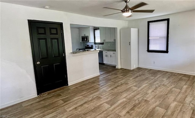 kitchen with stainless steel appliances, wood finished floors, a ceiling fan, baseboards, and decorative backsplash