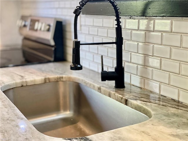 room details with decorative backsplash, light stone countertops, and a sink