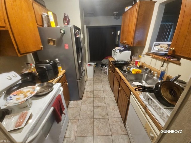 kitchen with white electric stove, brown cabinetry, a sink, and stainless steel fridge