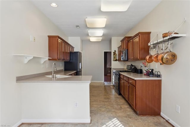 kitchen featuring a sink, a peninsula, light countertops, baseboards, and appliances with stainless steel finishes