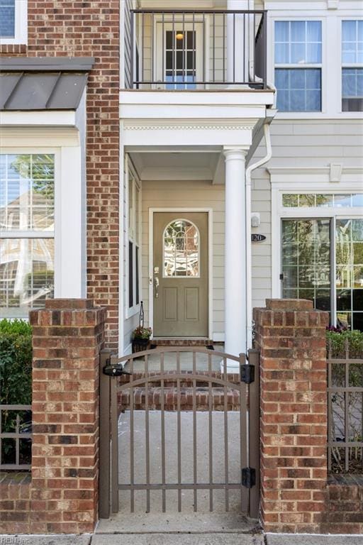 property entrance with brick siding, a balcony, and fence