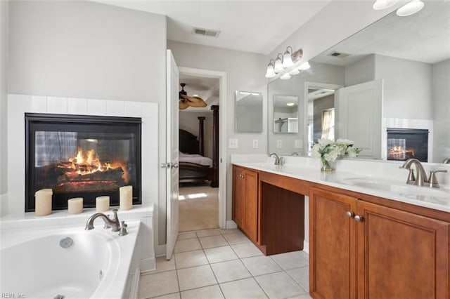 full bathroom featuring a glass covered fireplace, double vanity, a garden tub, and a sink