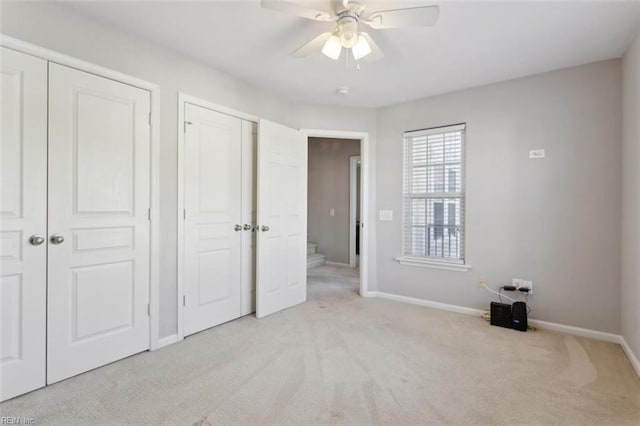 unfurnished bedroom with two closets, ceiling fan, light carpet, and baseboards