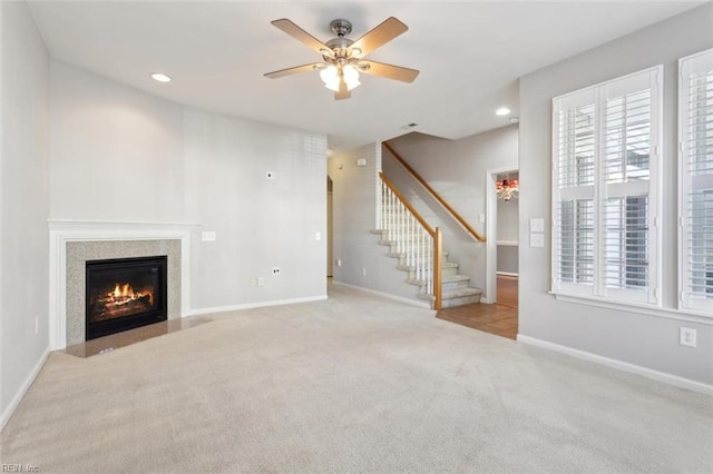 unfurnished living room with a high end fireplace, a ceiling fan, baseboards, carpet flooring, and stairs
