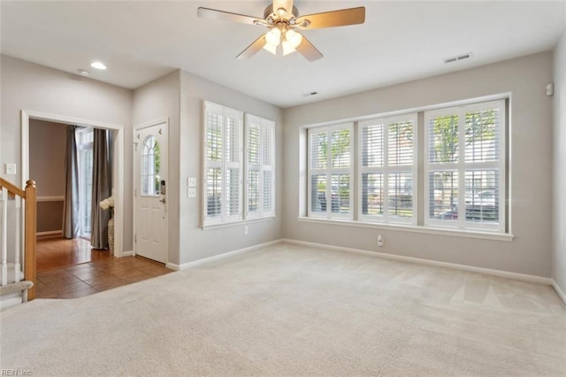 carpeted empty room featuring tile patterned floors, visible vents, baseboards, stairs, and ceiling fan