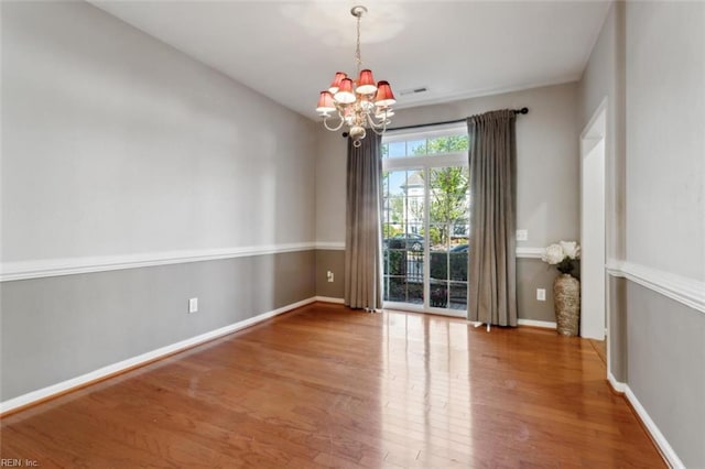 spare room with wood finished floors, visible vents, baseboards, and a notable chandelier