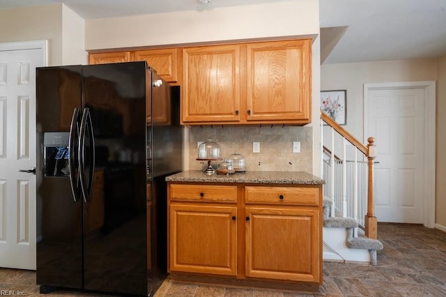 kitchen featuring brown cabinets, tasteful backsplash, light stone counters, and black fridge