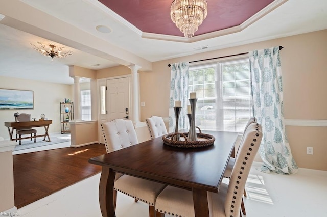 dining space featuring wood finished floors, a chandelier, a raised ceiling, visible vents, and ornate columns