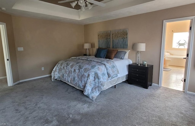 carpeted bedroom featuring a raised ceiling, baseboards, ceiling fan, and connected bathroom