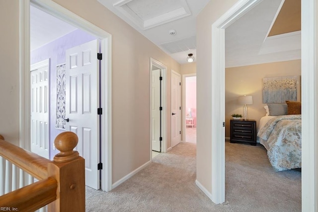 hallway featuring attic access, light carpet, and baseboards