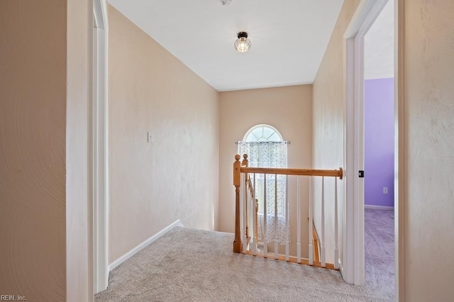 hallway featuring carpet, baseboards, and an upstairs landing