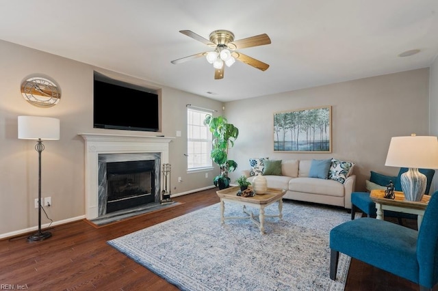 living area featuring a ceiling fan, baseboards, a high end fireplace, and dark wood-style flooring