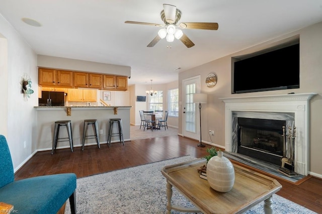 living area with dark wood finished floors, baseboards, a high end fireplace, and ceiling fan with notable chandelier