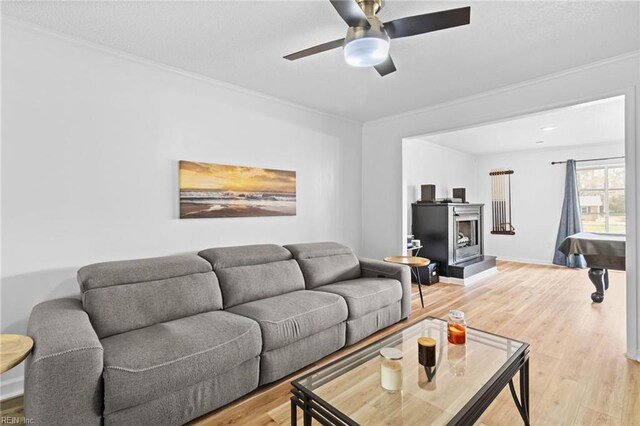living area with crown molding, a ceiling fan, baseboards, and light wood-style flooring