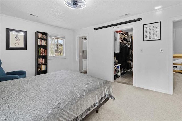 carpeted bedroom featuring a walk in closet, a closet, a textured ceiling, and ornamental molding