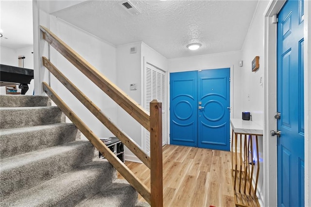 entrance foyer featuring stairway, a textured ceiling, visible vents, and light wood-style flooring