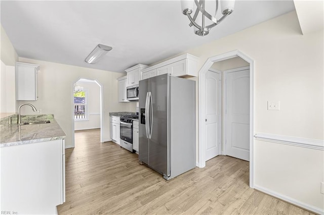 kitchen featuring white cabinets, a sink, arched walkways, light wood-style floors, and appliances with stainless steel finishes