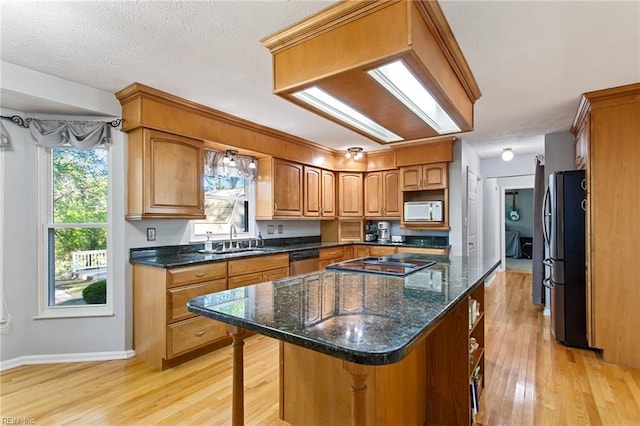 kitchen with stainless steel dishwasher, white microwave, light wood-style flooring, a kitchen bar, and freestanding refrigerator