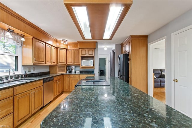 kitchen featuring brown cabinetry, appliances with stainless steel finishes, dark stone counters, and a sink