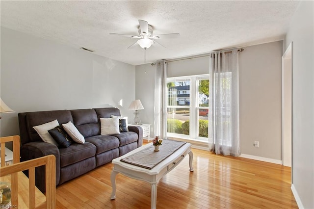 living area with light wood finished floors, visible vents, a ceiling fan, baseboards, and a textured ceiling