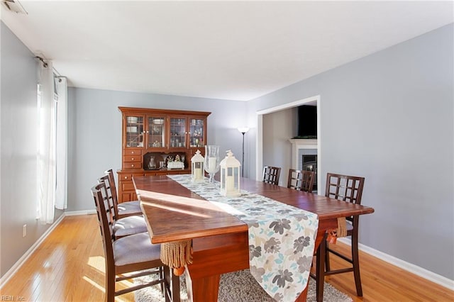 dining space with baseboards, visible vents, light wood finished floors, and a fireplace