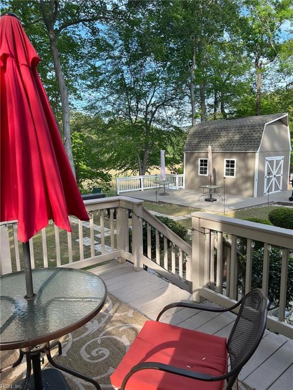 wooden terrace featuring outdoor dining area, an outbuilding, and a storage unit