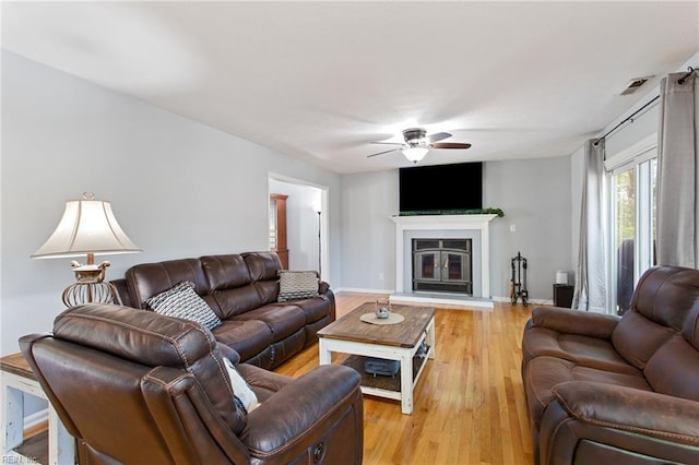 living room with a glass covered fireplace, light wood finished floors, a ceiling fan, and baseboards