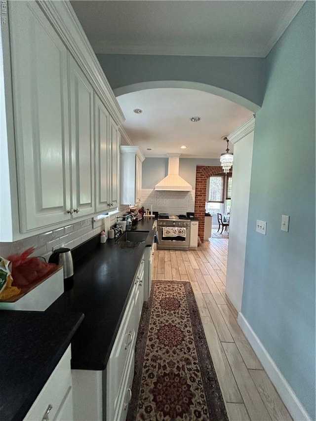 hallway with ornamental molding, baseboards, arched walkways, a sink, and light wood finished floors