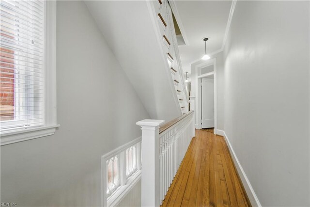 hallway featuring crown molding, baseboards, light wood-style flooring, and an upstairs landing