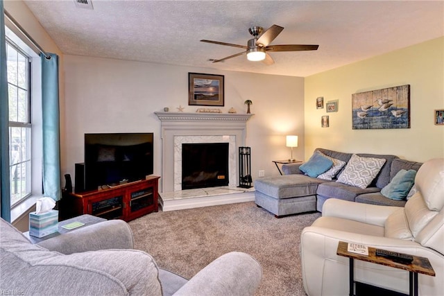 carpeted living area featuring a high end fireplace, a ceiling fan, a textured ceiling, and a healthy amount of sunlight