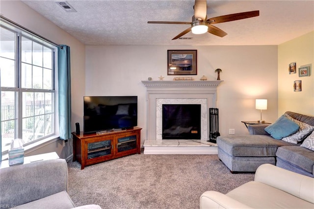 living room featuring carpet, visible vents, a ceiling fan, a premium fireplace, and a textured ceiling