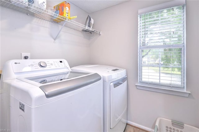 clothes washing area with baseboards, washing machine and clothes dryer, laundry area, and a wealth of natural light