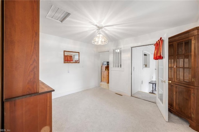 spare room featuring light carpet, french doors, visible vents, an inviting chandelier, and baseboards