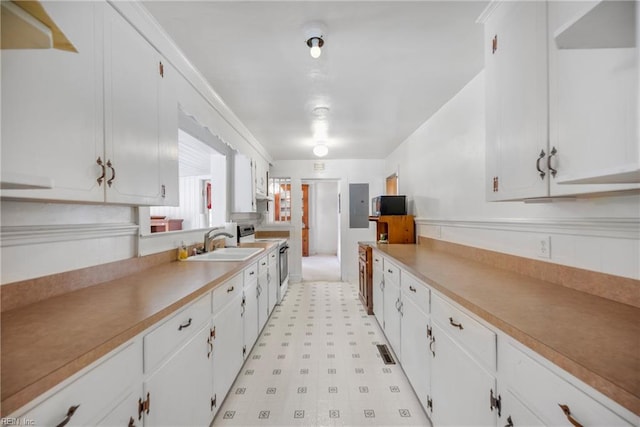 kitchen with light floors, range with electric stovetop, white cabinetry, and a sink