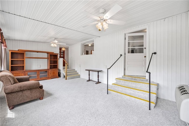 carpeted living room with wooden walls, stairs, and ceiling fan