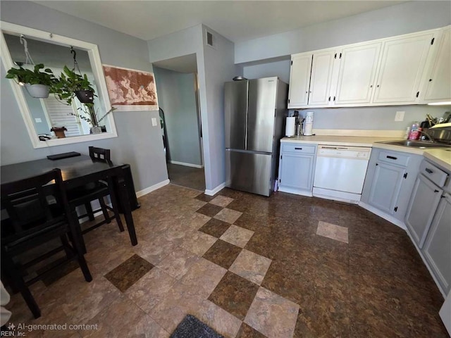kitchen featuring white dishwasher, a sink, light countertops, baseboards, and freestanding refrigerator