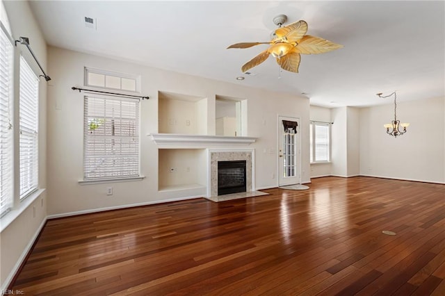 unfurnished living room with hardwood / wood-style floors, ceiling fan with notable chandelier, a tiled fireplace, baseboards, and visible vents
