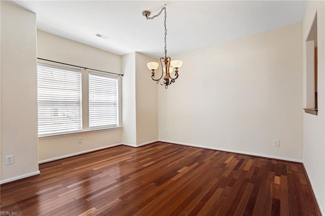 empty room with a chandelier, wood finished floors, visible vents, and baseboards