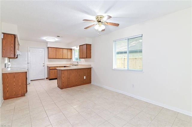 kitchen featuring a ceiling fan, brown cabinetry, a peninsula, light countertops, and baseboards