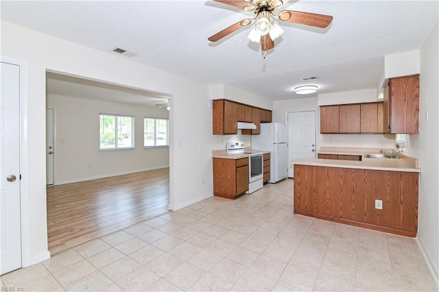 kitchen featuring brown cabinets, under cabinet range hood, visible vents, white appliances, and open floor plan