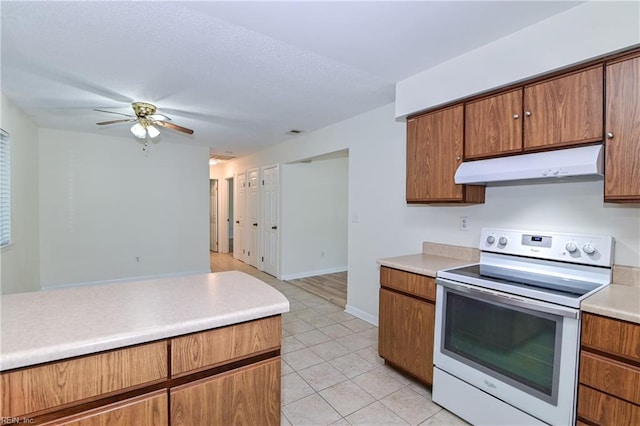 kitchen with a ceiling fan, brown cabinets, light countertops, under cabinet range hood, and electric stove