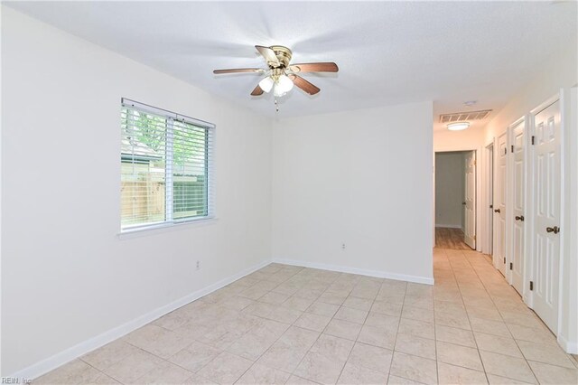 spare room with light tile patterned flooring, visible vents, a ceiling fan, and baseboards