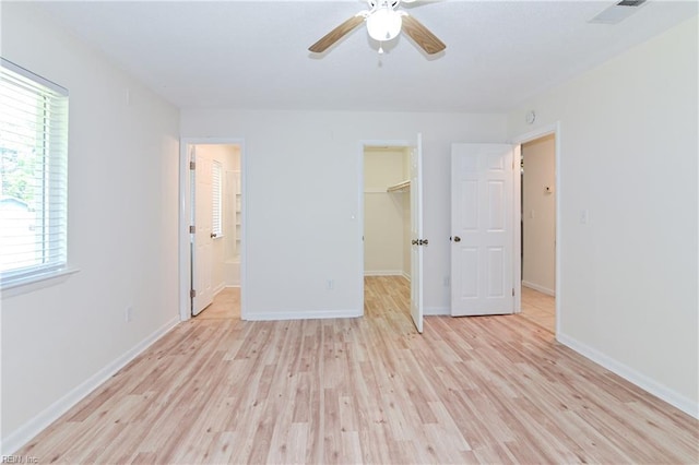 unfurnished bedroom featuring a closet, a walk in closet, light wood finished floors, baseboards, and visible vents