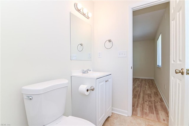 half bath featuring toilet, vanity, wood finished floors, and baseboards