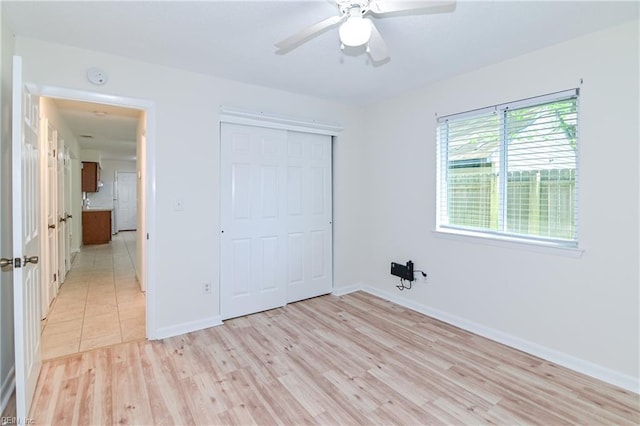unfurnished bedroom with a closet, light wood finished floors, baseboards, and a ceiling fan