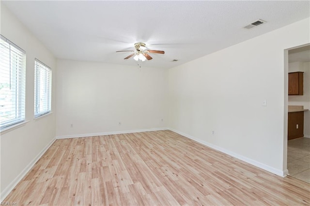 unfurnished room with light wood-type flooring, baseboards, visible vents, and ceiling fan