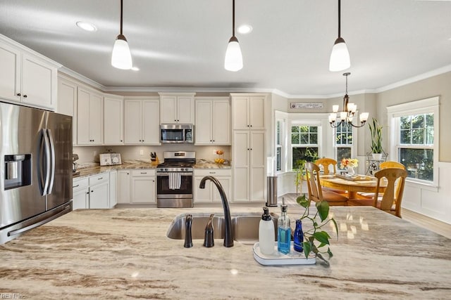 kitchen with light wood finished floors, light stone counters, ornamental molding, a chandelier, and appliances with stainless steel finishes